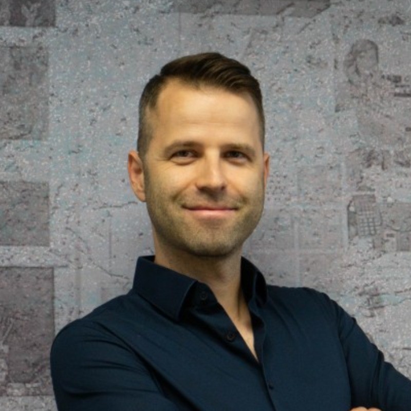 Danijel Senekovic portrait - a man standing in front of a wall, smiling.